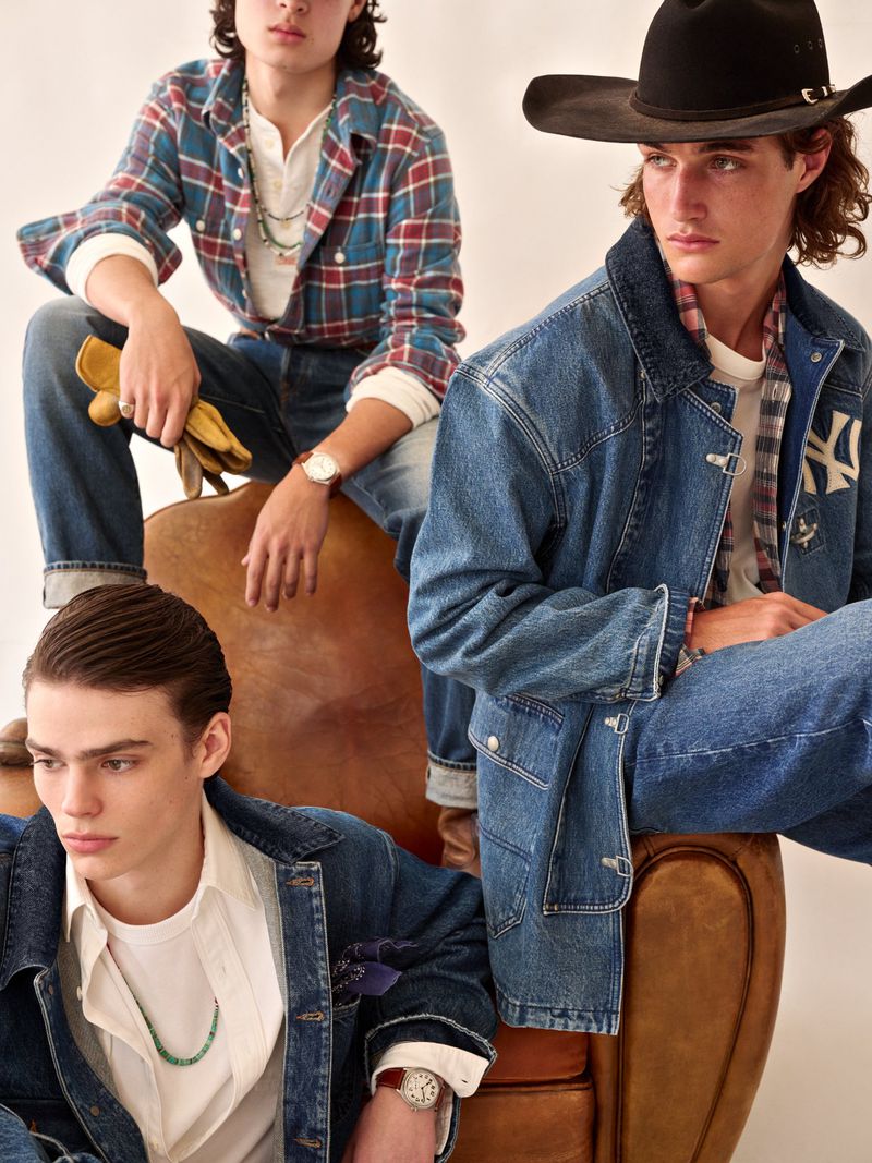 Three young adult men in Western-inspired denim fashion sit on and around a vintage leather chair in a studio setting.