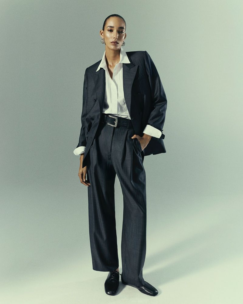 Fashionable woman in grey suit and white shirt strikes a pose against a neutral backdrop, showcasing modern elegance and style.