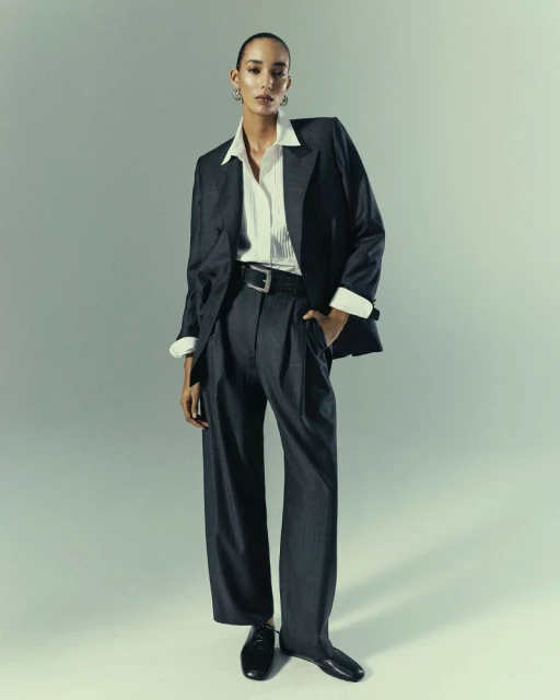 Fashionable woman in grey suit and white shirt strikes a pose against a neutral backdrop, showcasing modern elegance and style.