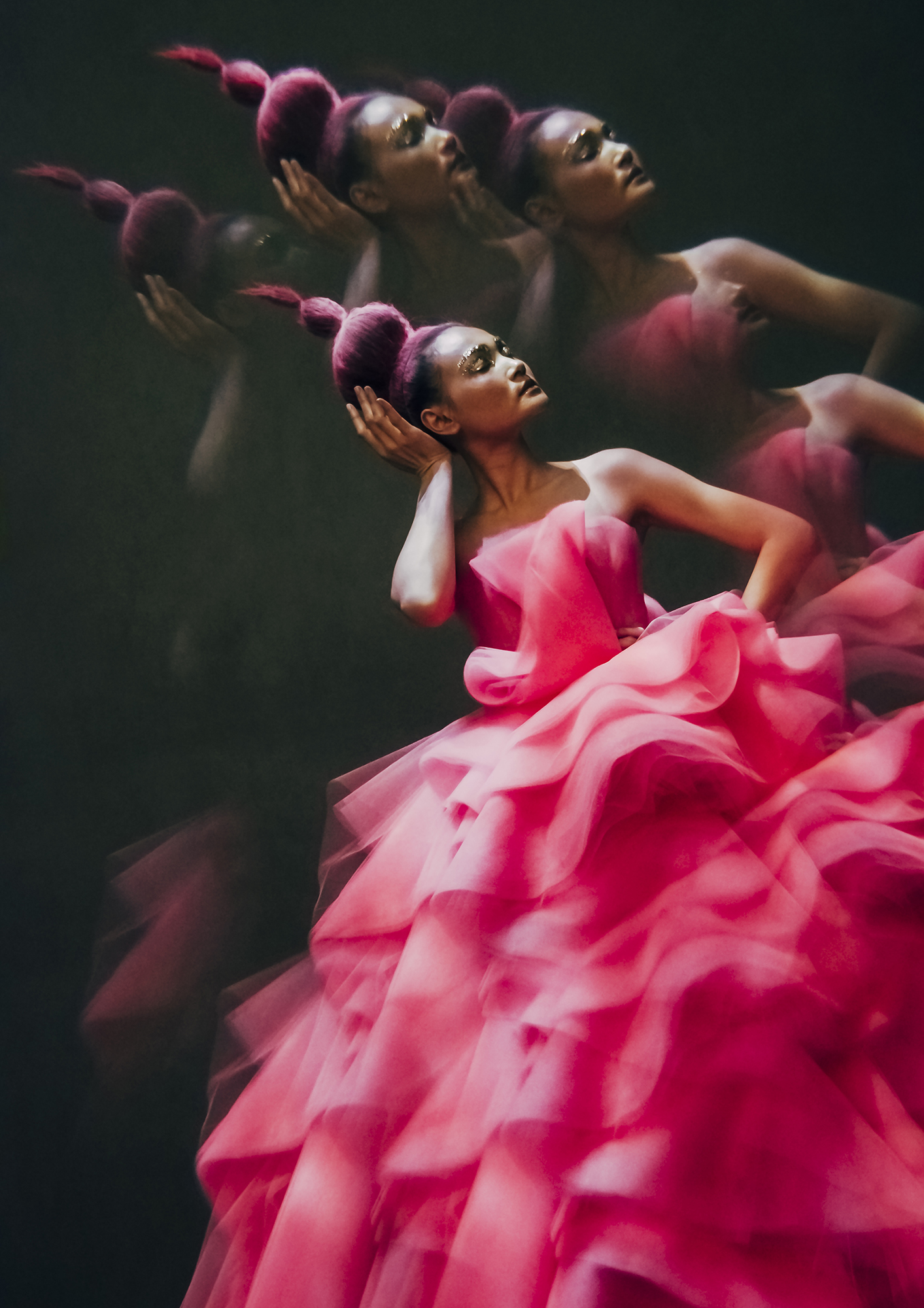 Woman in a pink gown with motion blur, posing with her hand on her head against a dark background. Fashion and glamour photography.