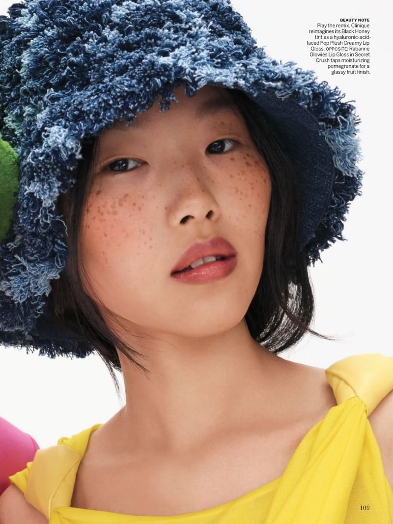 Close-up portrait of an Asian woman wearing a blue denim bucket hat and a yellow top, posing against a white backdrop in a photo studio.