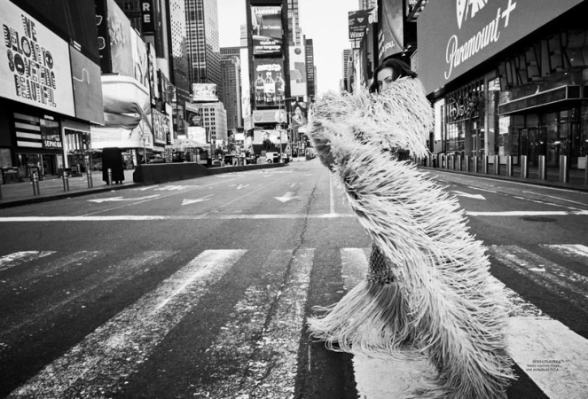 A woman in a flowing fringed garment stands in the middle of an empty Times Square street in New York City. Black and white photography.