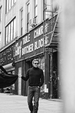 Man walks past a Chef Butcher Block restaurant supply store, wearing a black turtleneck, jeans, and sunglasses on a city street.