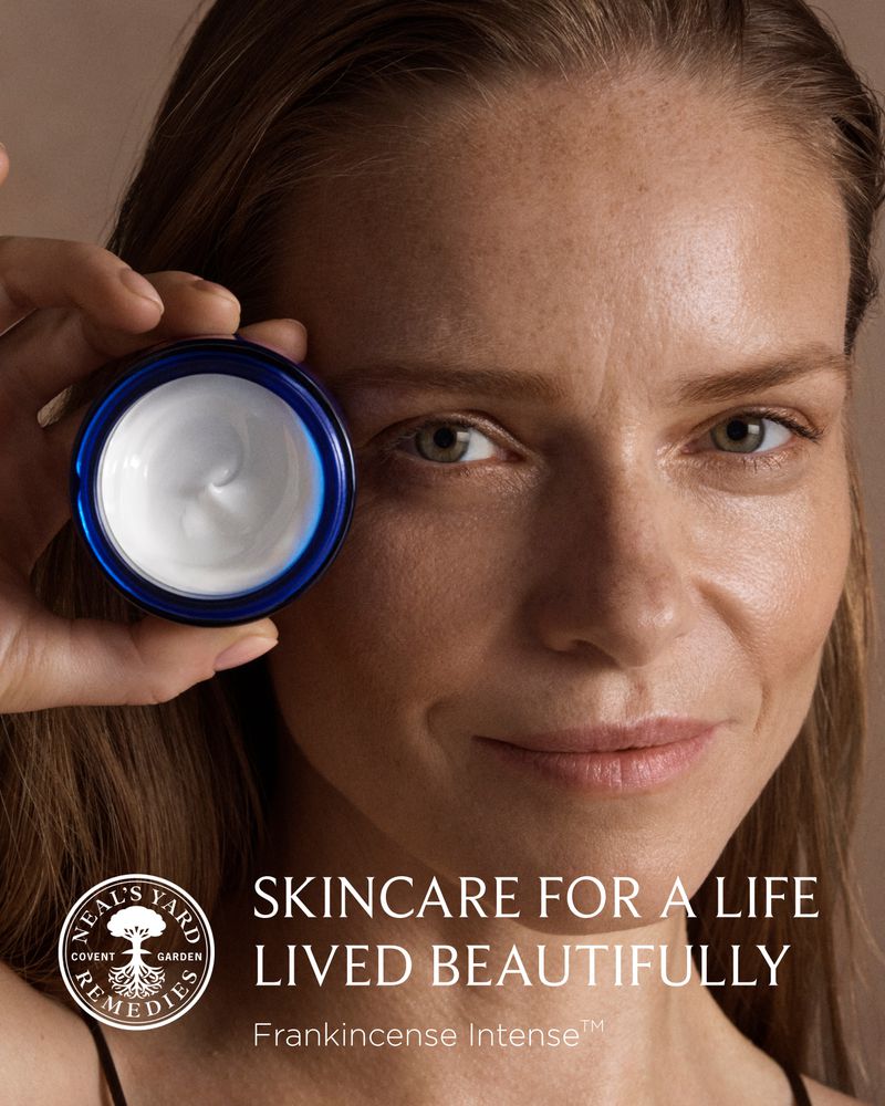 Close-up of a woman holding a jar of skincare cream. The woman is fair-skinned, with light brown hair and light-colored eyes.