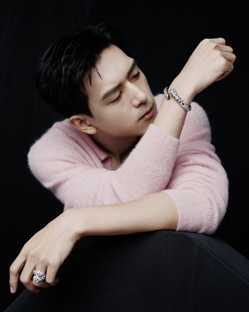 Portrait of a handsome Asian man in a pink sweater, with jewelry, posing against a dark background in a visually appealing composition.