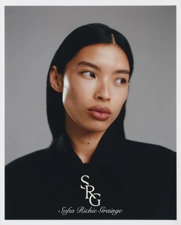 Close-up portrait of a woman with sleek dark hair and natural makeup against a plain grey studio backdrop with white border.