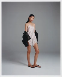 Model in pink lace slip dress wearing a black leather jacket against a grey studio backdrop