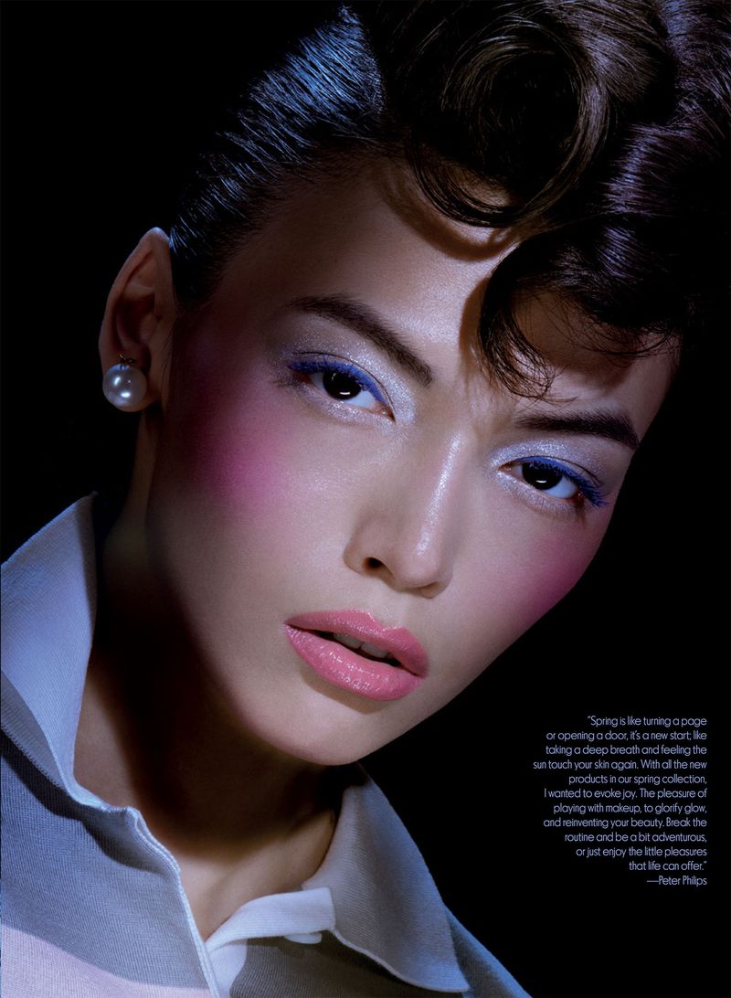 Close-up fashion shot of an Asian woman with makeup and styled hair in a white polo shirt against a dark backdrop.