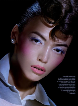 Close-up fashion shot of an Asian woman with makeup and styled hair in a white polo shirt against a dark backdrop.