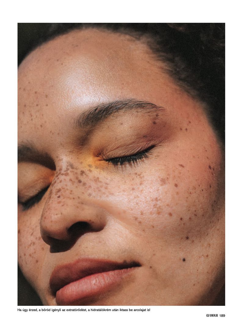 Close-up portrait of an adult woman with freckles and closed eyes, showcasing natural beauty and skin texture in soft, diffused lighting.