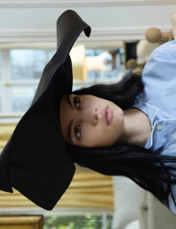 Model wearing a large black sculptural hat and light blue shirt in an indoor setting photographed for 10 Magazine