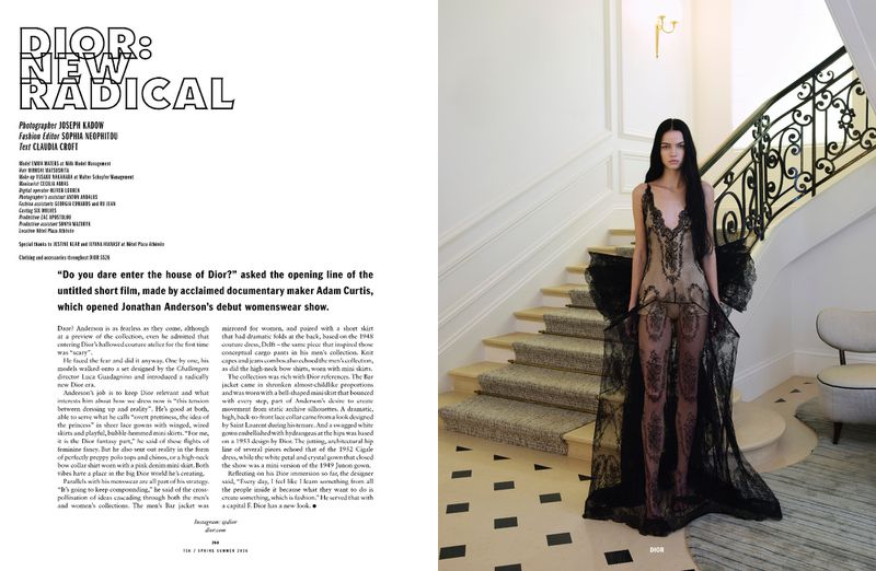 Fashion editorial shot of a slender adult woman with long dark hair wearing a sheer black lace gown, standing on a marble staircase indoors.