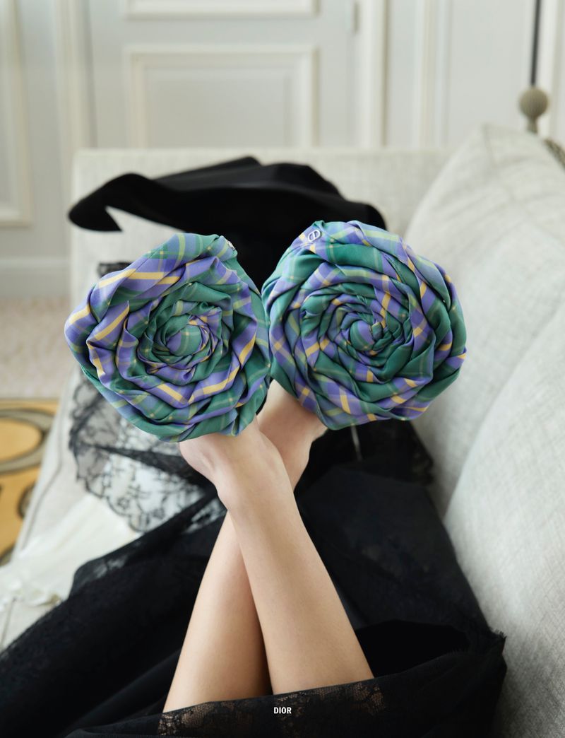 Two tie roses held by a fair-skinned person, with a black hat and lace visible. The roses have a green, purple, and yellow plaid pattern.