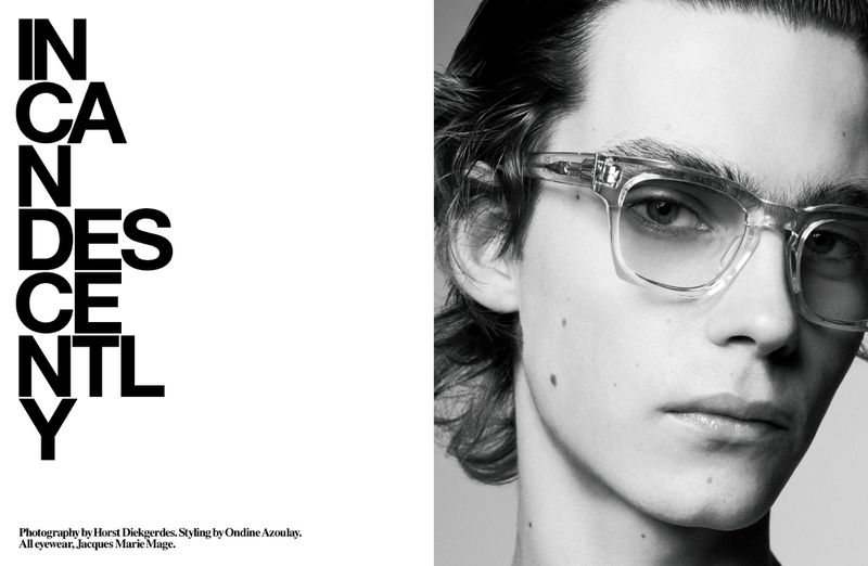 Monochrome close-up of a fair-skinned adult male model wearing transparent glasses, with a vertical text block to the left.