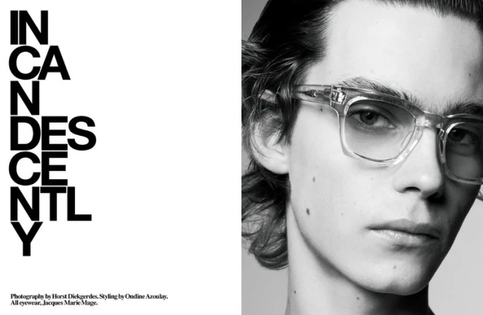 Monochrome close-up of a fair-skinned adult male model wearing transparent glasses, with a vertical text block to the left.