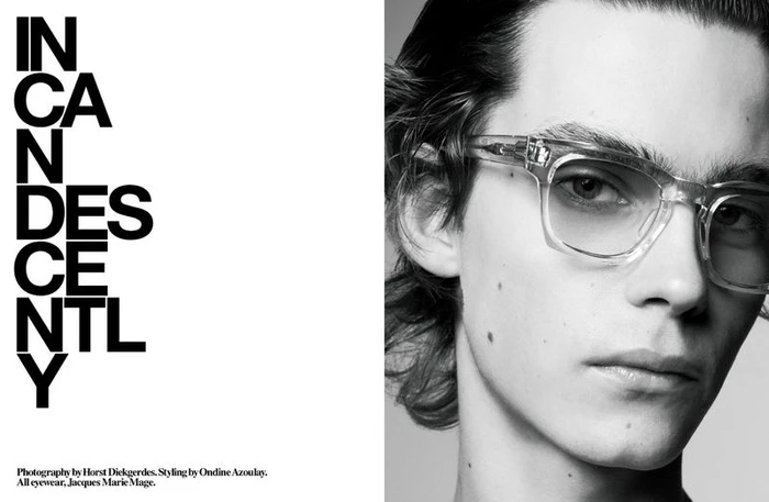 Close-up black and white portrait of a young male model wearing clear acetate eyeglasses against a plain background