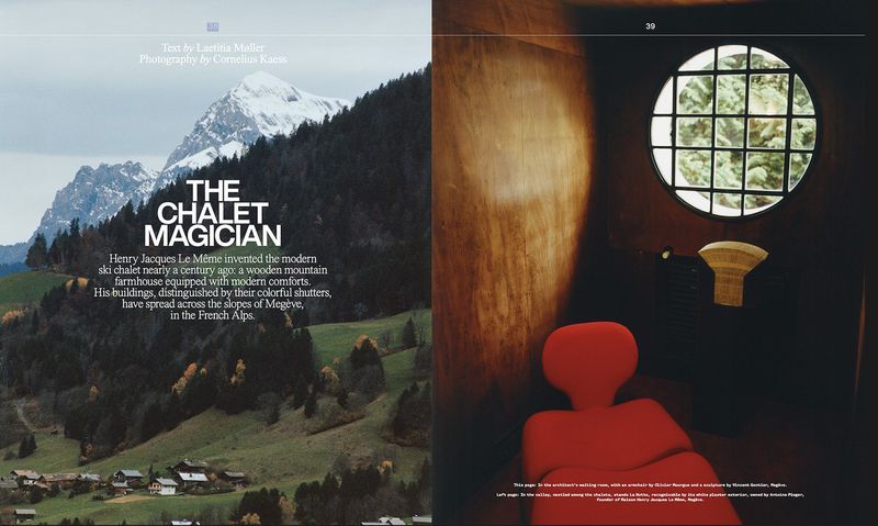 Landscape shot showcases a chalet on a mountainside beside a red chair in a dimly lit room with a round window overlooking greenery.
