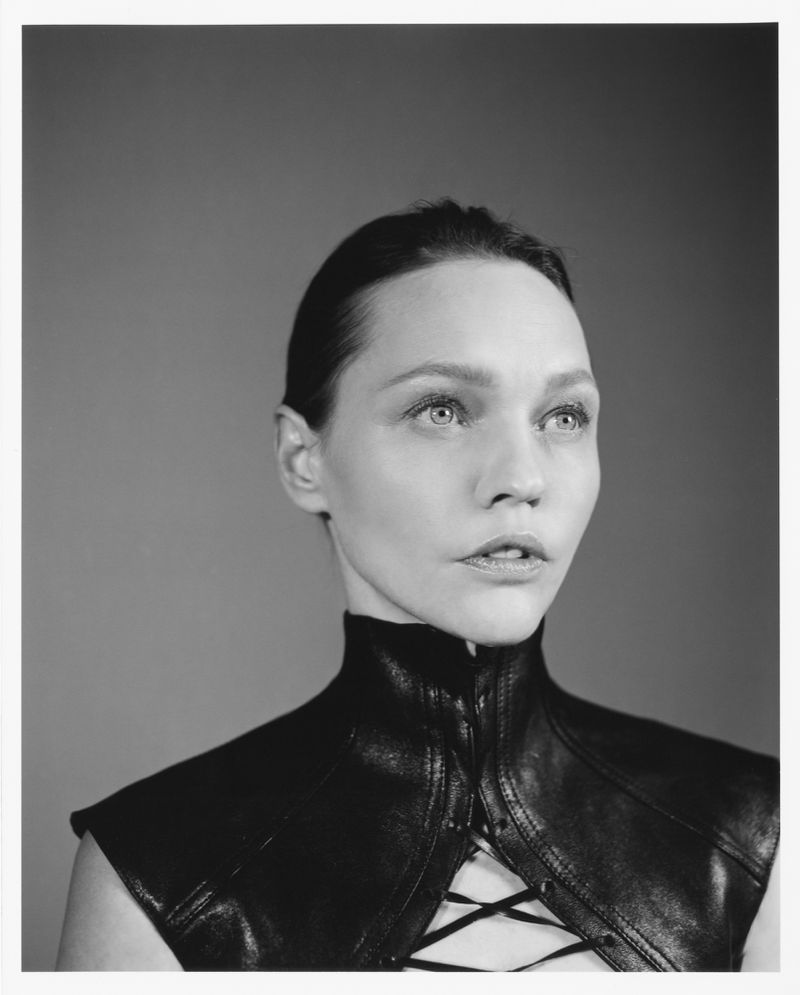 Monochrome portrait of a woman with fair skin wearing a black leather halter top, gazing to the side against a plain background.