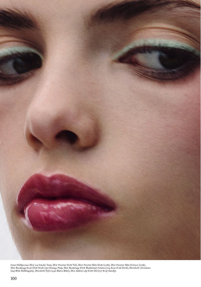 Close-up shot of a model's face showcasing glossy lips, mint eyeliner, and flawless skin, emphasizing beauty and makeup details.