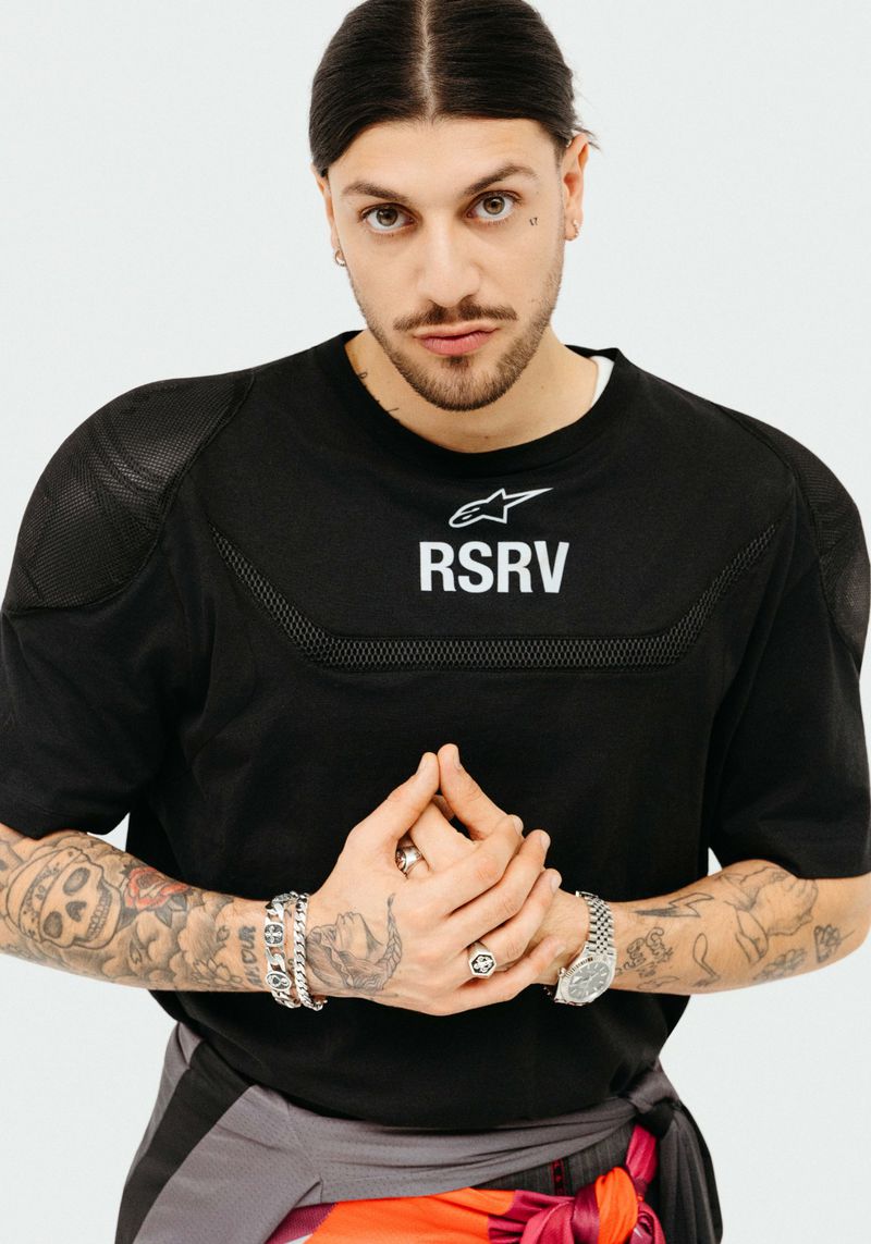 Man with tattoos wearing a black t-shirt with text against a white background for Lui Magazine France photographed by Stéphanie Volpato.
