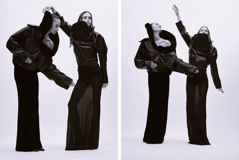 Two fashion models strike a pose in black gowns and jackets in a studio environment, showcasing bold and unconventional design elements.
