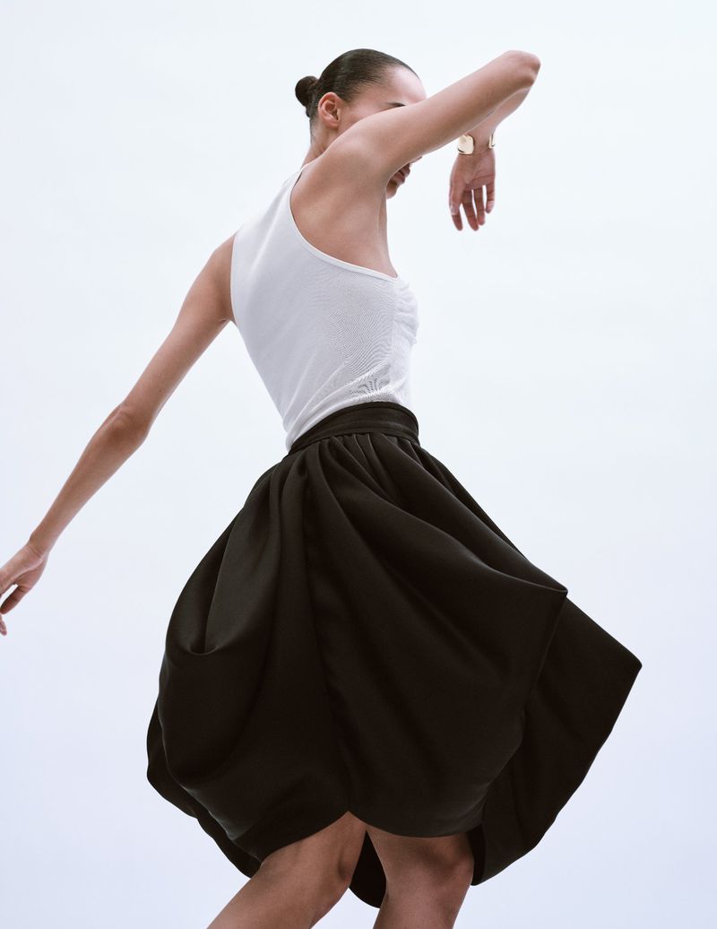 Elegant studio fashion shot featuring a female model in a white top and black skirt, gracefully posed against a bright white backdrop.