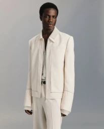 Model wearing a cream-colored zip jacket and matching trousers against a neutral grey studio background