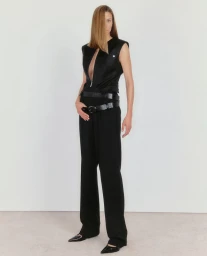Model wearing a black sleeveless top with a deep zipper cutout and black trousers against a neutral background