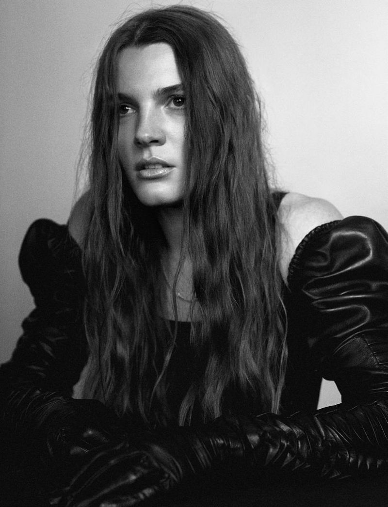 Black and white portrait of a woman with long hair wearing black puffed-sleeve gloves and top against a neutral background.