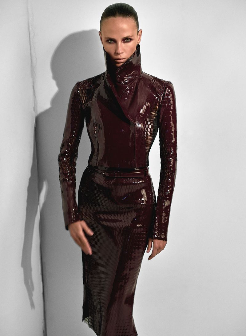 Woman poses in a shiny, dark red, reptile-patterned dress in a minimalist photo studio setting with a modern, high-fashion aesthetic.