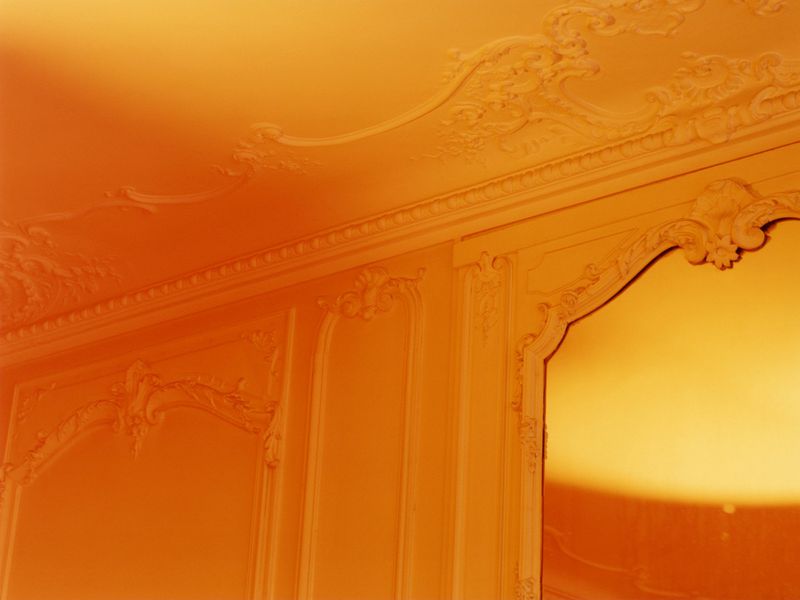 Ornate wall and ceiling with decorative plasterwork, featuring paneling and arches, illuminated by warm, diffused orange and yellow lighting.