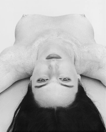 Black and white studio shot features a woman's face and upper body, shown upside down against a plain backdrop, emphasising her features.