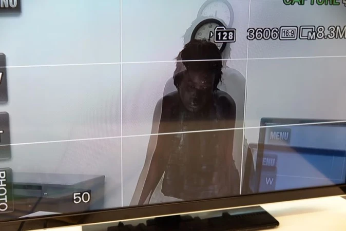 On a monitor screen, an adult female appears centered within framing guides, with technical information, a clock, and menu options visible.