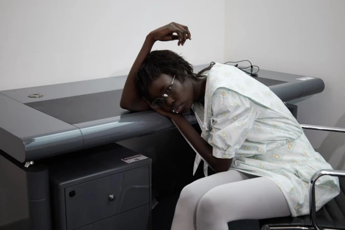 Model Tessa Jean resting head on large grey desk in white office interior