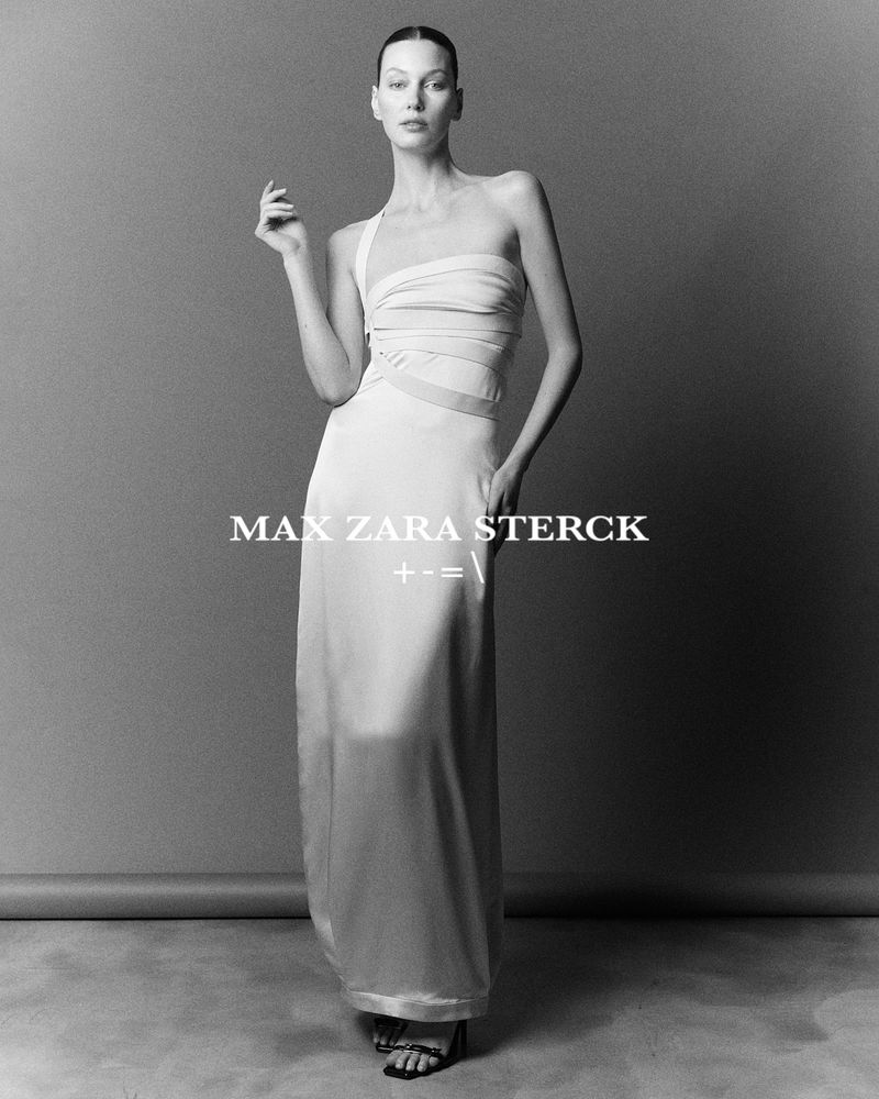 Black-and-white fashion shot of a slender woman in a flowing gown, posing against a neutral backdrop in a photo studio setting.
