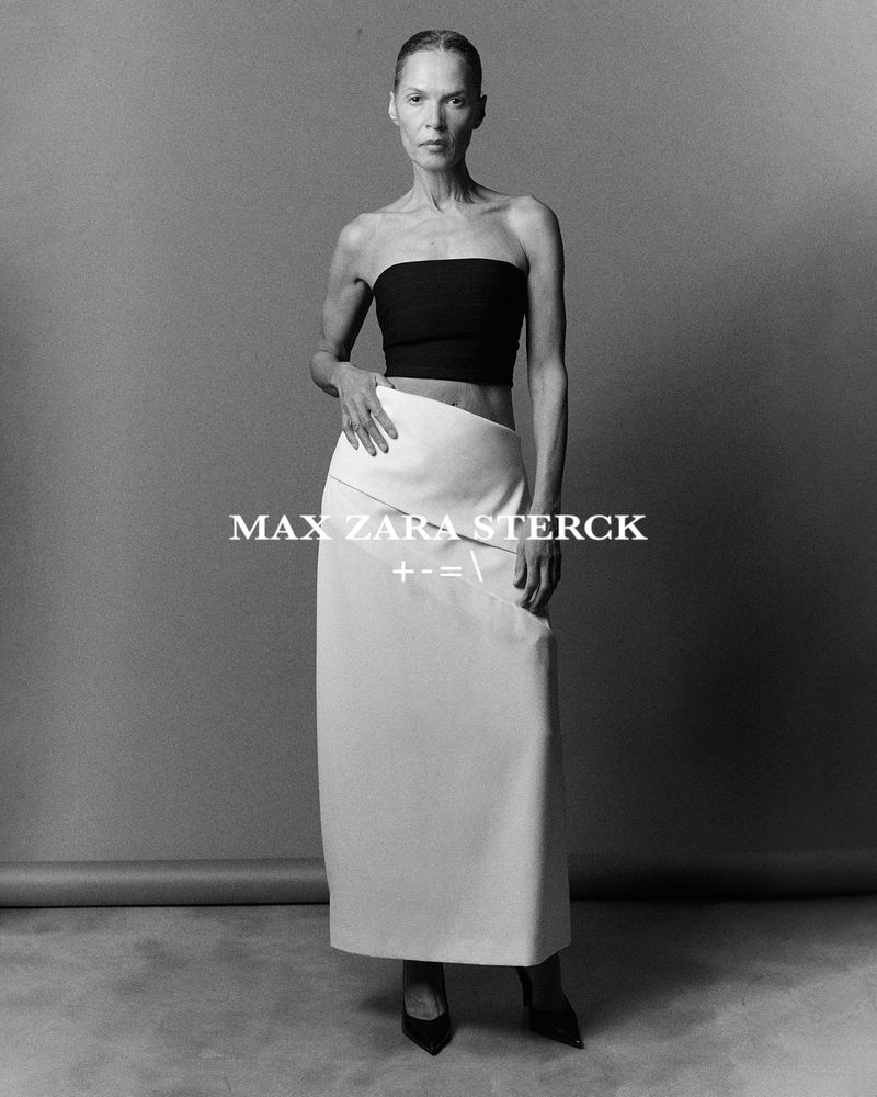 Black and white fashion shot of a woman wearing a tube top and a long skirt in a studio. The model poses with one hand on her skirt.