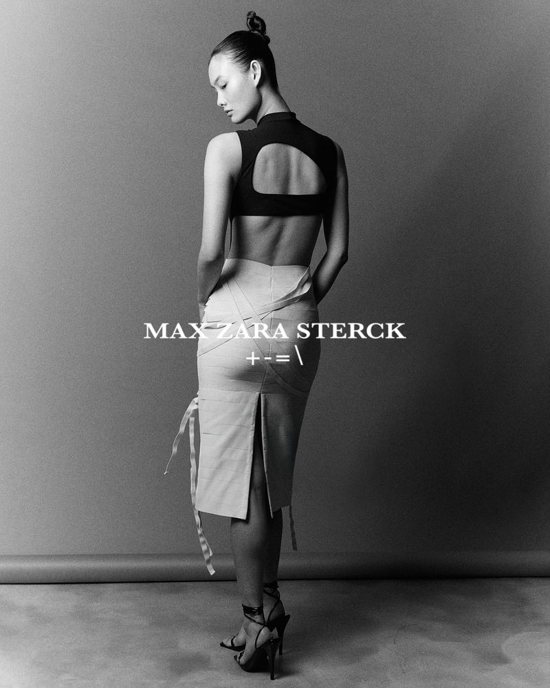 Asian woman poses in black top and tan skirt in a studio. Back view portrait fashion shot in black and white with cool tones.