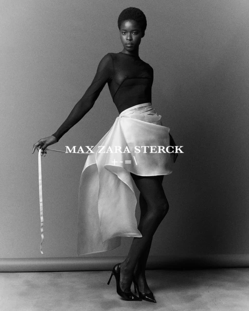 Elegant studio shot of an African American fashion model in a sheer black top and flowing white skirt, posing against a gray backdrop.