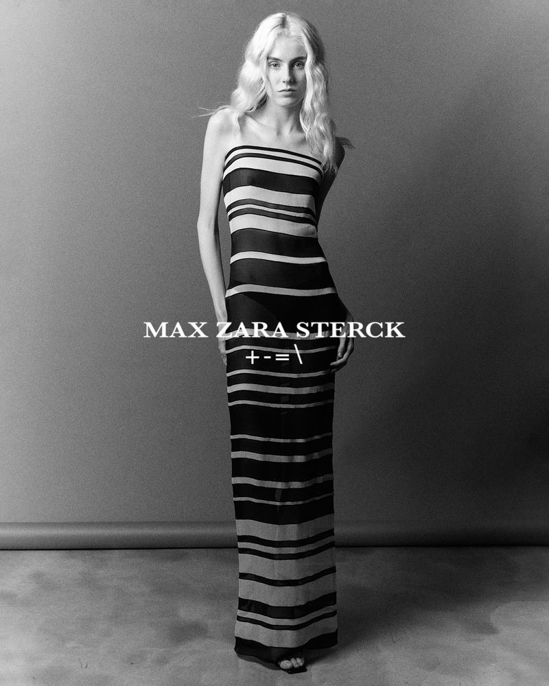 Model standing in a monochrome striped strapless maxi dress against a dark neutral studio backdrop.