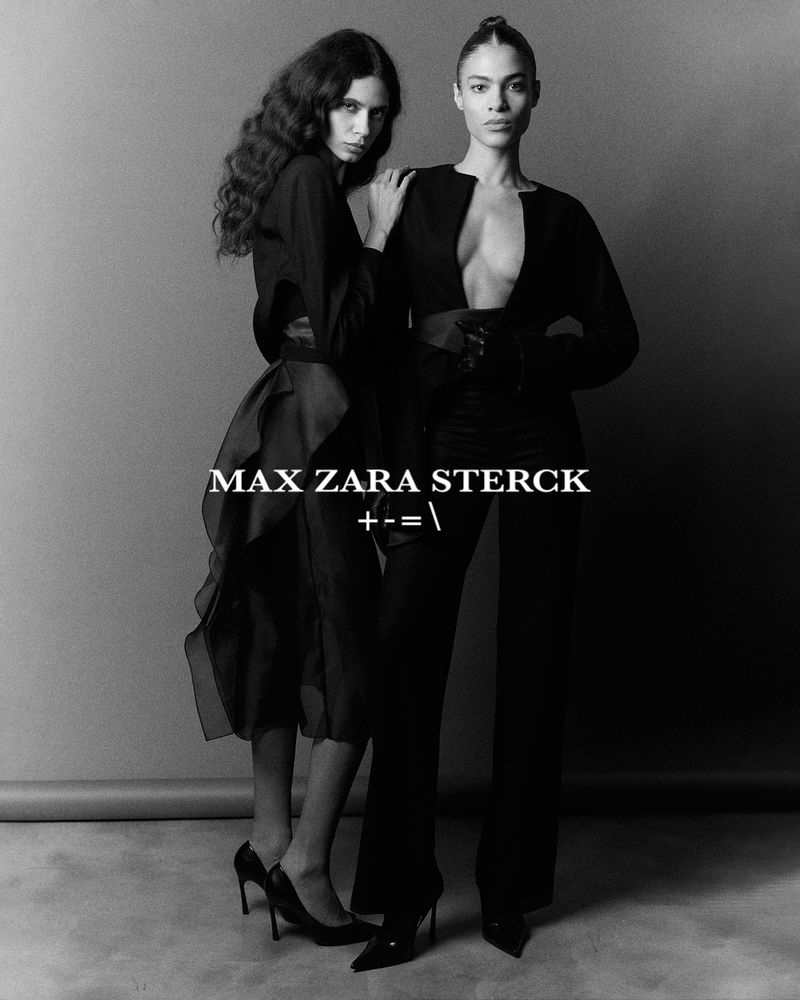 Two fashion models pose in black attire against a gray backdrop, showcasing sleek, high-fashion style in a studio environment.