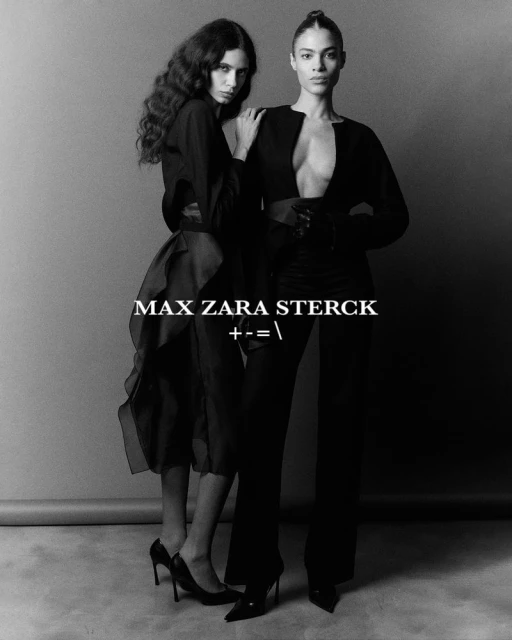 Two fashion models pose in black attire against a gray backdrop, showcasing sleek, high-fashion style in a studio environment.