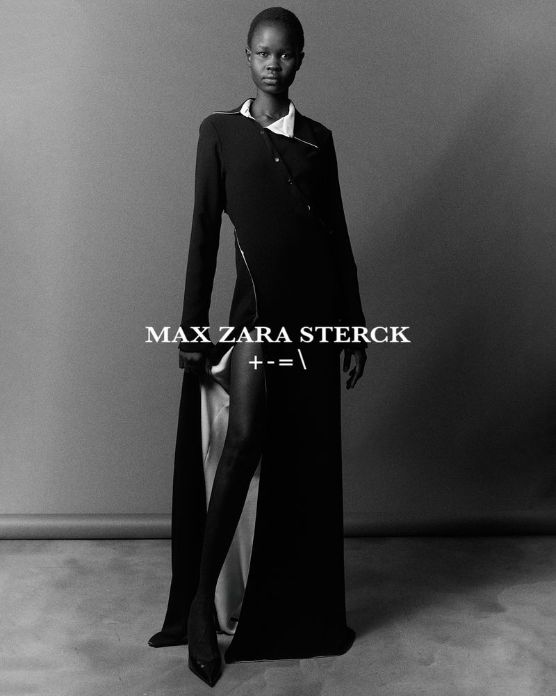 Black-and-white portrait of an African woman in a dark, asymmetrical dress and black heels, posed against a neutral grey background.