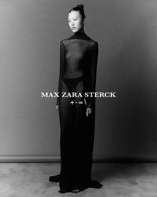 Black and white studio shot of an Asian woman in a black sheer gown, standing in a full shot with neutral gray background and floor.