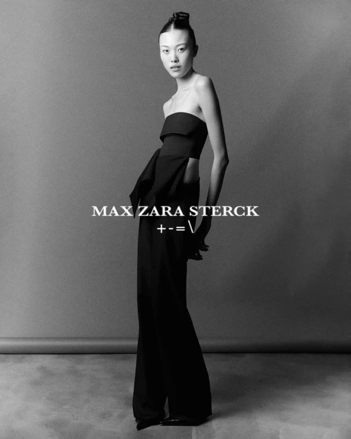 A stylish Asian woman poses in a strapless black top and wide-leg pants against a gray backdrop in a studio, showcasing a minimalist fashion look.