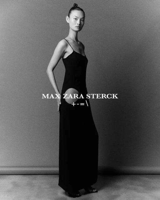 Studio shot of a female fashion model in a black floor-length dress with cut-out, posing against a grey backdrop.