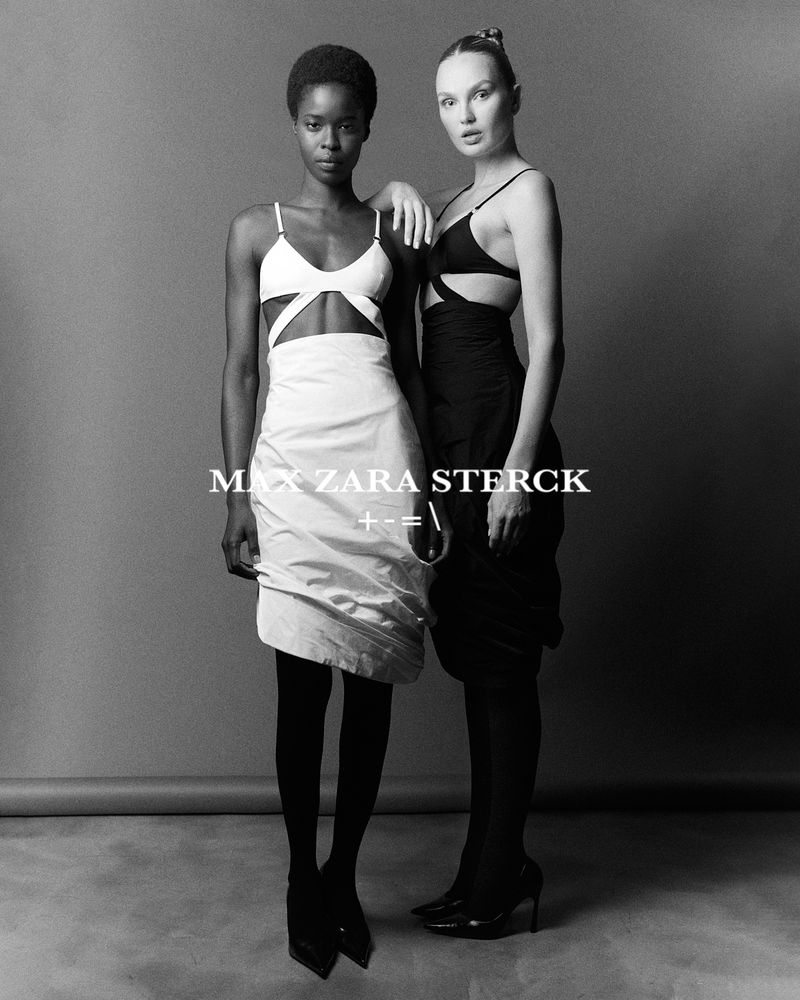 Two women in black and white minimalist fashion. One has her arm on the other's shoulder in a studio setting, monochrome color grading.