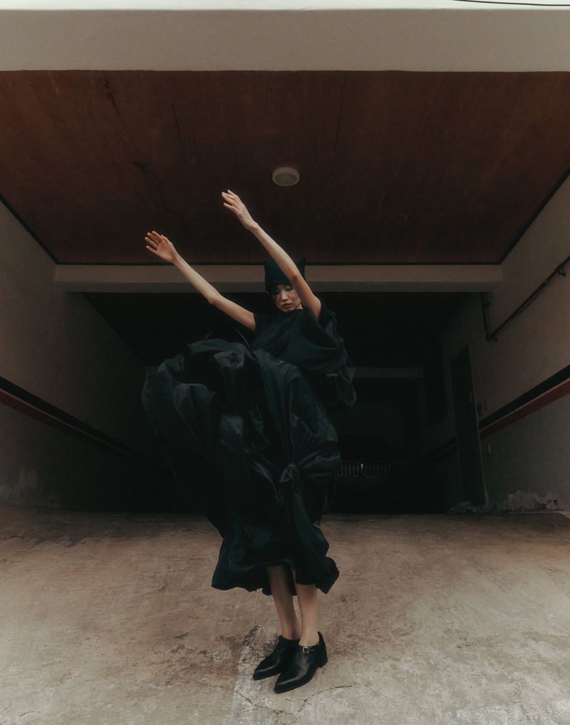 Model in a flowing black dress dancing with arms raised inside a covered garage entryway