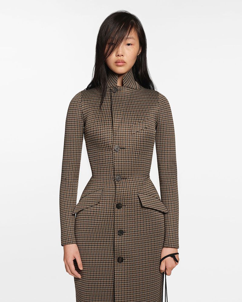 Portrait of an adult woman wearing a houndstooth print dress with long sleeves posing against a white studio backdrop.