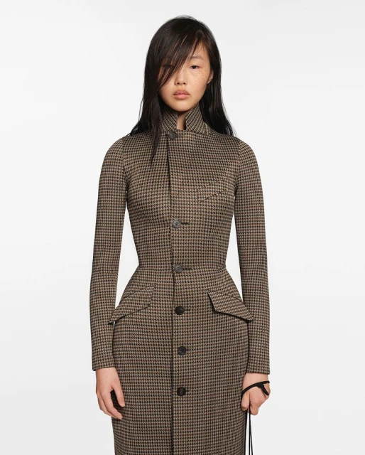 Portrait of an adult woman wearing a houndstooth print dress with long sleeves posing against a white studio backdrop.