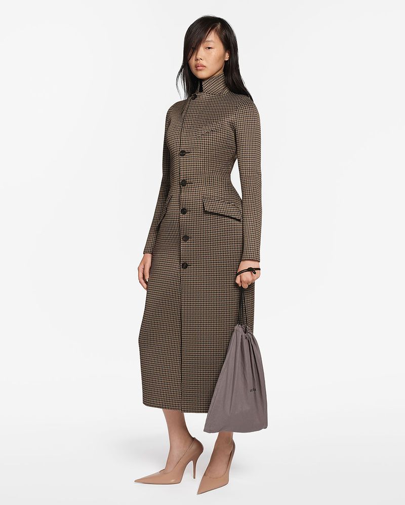 A slender Asian female model showcases a long-sleeved brown and black houndstooth dress, paired with beige heels and a grey drawstring bag.